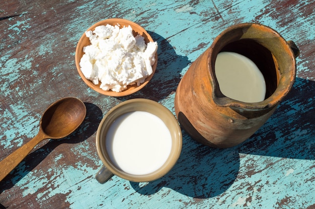 Tonkrug, eine Tasse Milch und Hüttenkäse auf einem Tisch aus hellblauen Brettern. Ansicht von oben