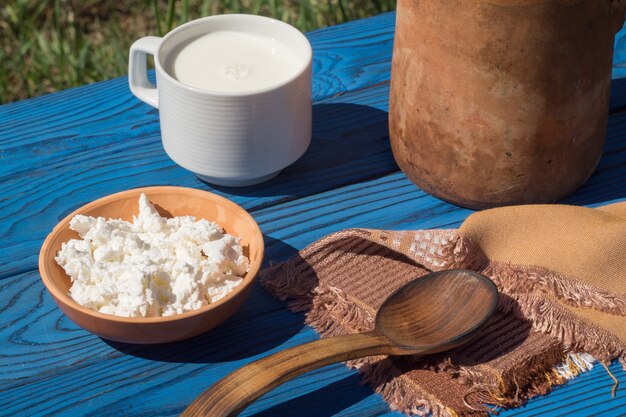 Tonkrug, Korb, eine Tasse Milch und Hüttenkäse auf einem Tisch aus blauen Brettern