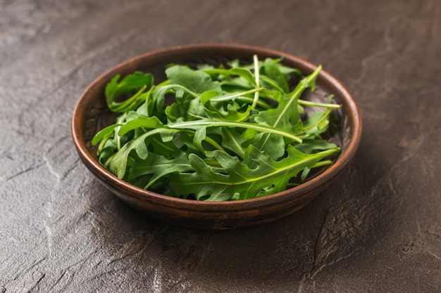 Tonschale mit frischem Rucola auf einem dunklen Steintisch. Gesunde pflanzliche Ernährung. Vegetarische Küche.