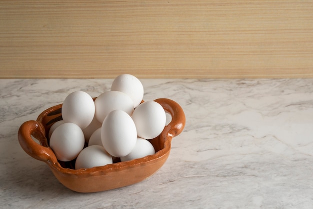 Tontopf gefüllt mit weißen Eiern auf Marmorstab und Holzboden