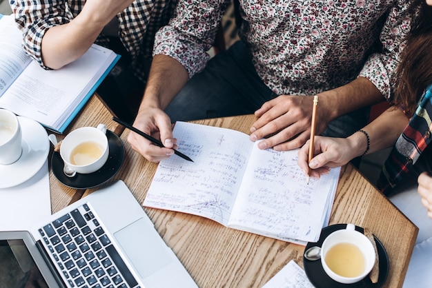 Top-Ansicht der Leute, die mit Copybook, Buch und Laptop studieren. Tasse Kaffee auf dem Tisch