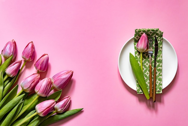 Foto top-ansicht der tischgestaltung mit teller und serviette in der nähe der tulpe auf dem rosa tisch