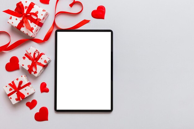 Top-Ansicht des digitalen Tablets mit Geschenkkisten und Herzen auf farbenfrohem Hintergrund Tablet mit schwarzem Bildschirm mit Urlaubsdekorationen Geschenkkiste Top-Anblick