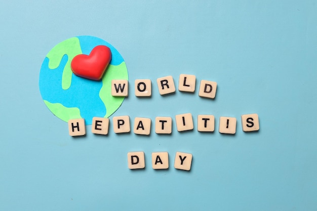 Top-Ansicht des Textes WELD HEPATITIS DAY auf Würfeln und Globus mit einem isolierten Herz auf blauem Hintergrund