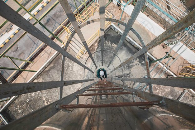 Foto top-ansicht männlicher arbeiter klettert auf die leiter inspektion edelstahl-tank arbeit in der höhe