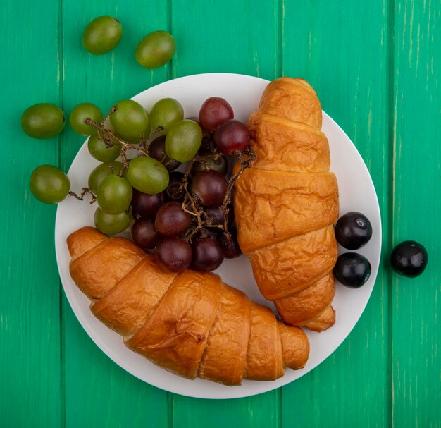 Top-Ansicht von Croissants und Trauben auf einem Teller auf grünem Hintergrund
