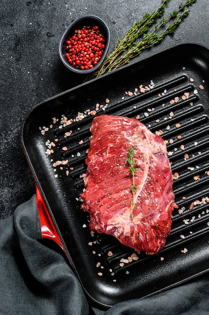 Top Blade Steak auf einer Grillpfanne, rohes Fleisch, marmoriertes Rindfleisch. Schwarzer Hintergrund. Draufsicht