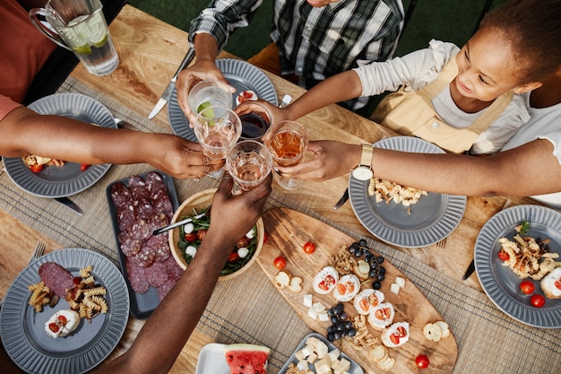 Top-Down-Porträt einer großen afroamerikanischen Familie, die beim gemeinsamen Abendessen draußen klirrt.