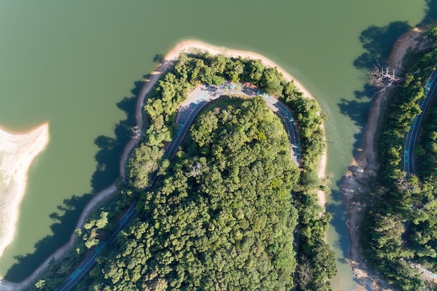 Top down von Drone Luftbild des Regenwaldes mit Asphaltstraße um den Damm und gemeinsamem Land Vorsicht Fahrradschild auf der Straße.