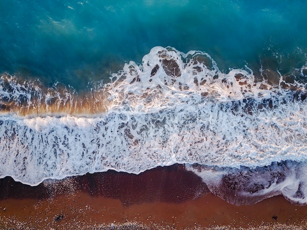 Top Fotoansicht von der fliegenden Drohne der exotischen Korallenseelandschaft mit türkisfarbenem klarem Wasser und Wellen, die sich dem Kiesstrand nähern.