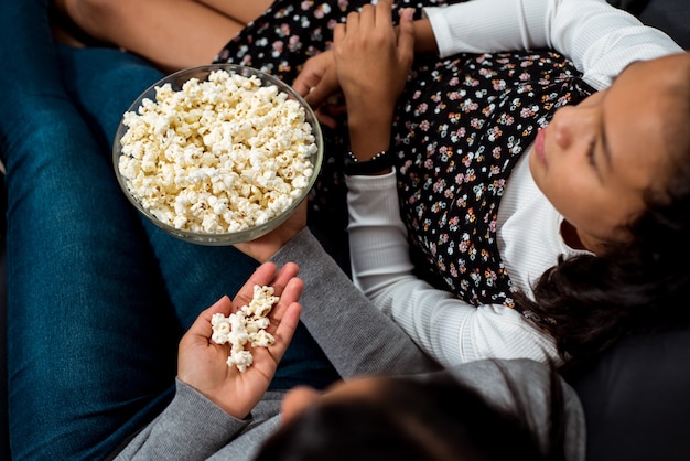 Top-Fotografie von zwei Mädchen, die sich in seiner Freizeit beim Fernsehen entspannen und Popcorn essen.