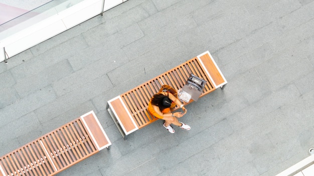 Top Luftaufnahme Mode Frau mit Einkaufstasche verwendet Smartphone sitzen auf Holzbank am Gehweg Fußgänger mit Unschärfe Menschen gehen