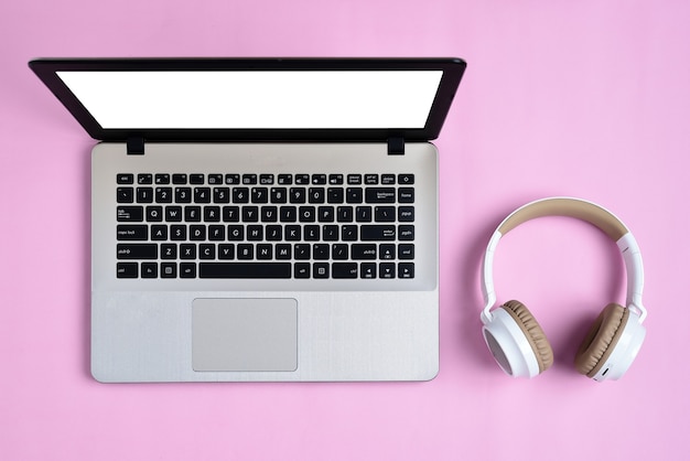 Top View Flatlay de fone de ouvido sem fio moderno e laptop minimalista com tela branca no espaço de trabalho cor de rosa