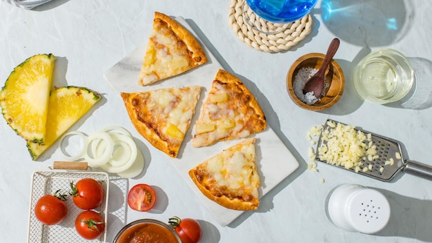 Foto top-view geschnitten dreieck stücke von köstlichen leckeren hausgemachten hawaiianischen traditionellen italienischen kruste dünnen knusprigen schinken und ananas pizza auf dem teller mit zutaten tomaten käse salz auf dem tisch