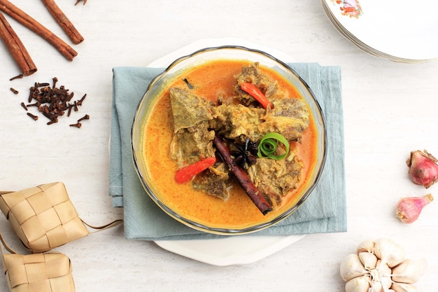 Top View Gulai Sapi ist Beef Curry typisch traditionelles Essen aus Padang, West Sumatera, Indonesien. Serviert am Tisch mit Schüssel und Ketupat Lebaran. Menü für Eid al Adha (Idul Adha).