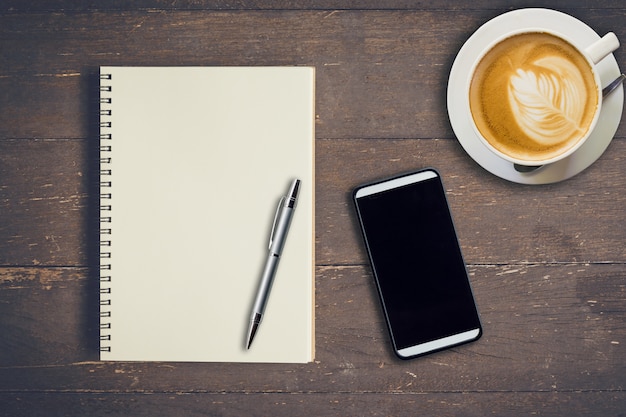 Top View Notebook, Kugelschreiber, Kaffeetasse und Telefon auf Holztisch, Vintage Filter.