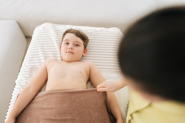 Top-View-Porträt eines fünfjährigen Jungen-Patienten mit therapeutischer Massage auf dem Bauch, der in einer medizinischen Klinik auf der Couch liegt