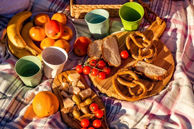 Foto top-view von gesundem picknick-essen auf einem holzbrett auf einer decke im freien bei sonnenuntergang an einem sonnigen sommertag