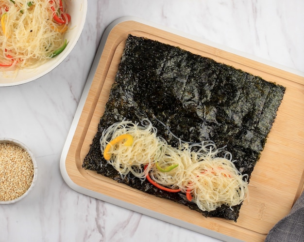 Top View Zutaten Herstellung von Gimmari oder Kimmari, Laver (Nori Algen) gefüllt mit Japchae (Stir Fry Glass Noodel). Beliebtes Snack Street Food in Südkorea. Schritt für Schritt