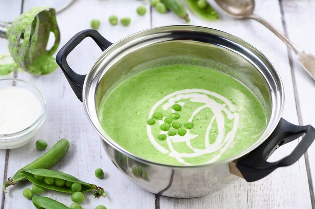 Topf mit frisch gekochter Suppe aus pürierten grünen Erbsen und Sahne auf dem Tisch.