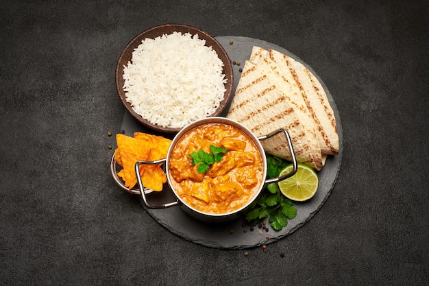 Topf mit traditioneller Hühnchen-Curry-Schüssel mit Reis und Pita auf Stein-Servierbrett