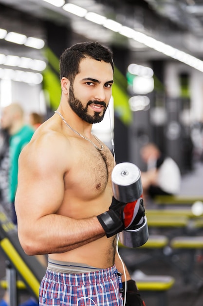 Topless bärtiger Mann hält Metallhantel im Fitnessstudio