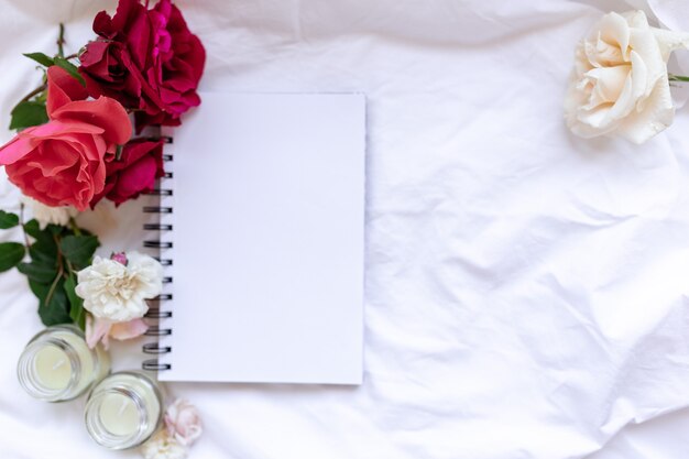 Topview elegante com flores de rosas da primavera, caderno e velas em uma folha amassada. Espaço para texto. Conceito de casa aconchegante