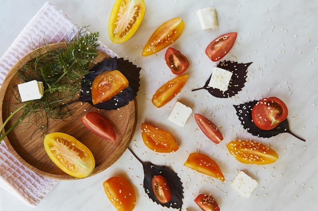 Un toque de ensalada de temporada saludable con tomates rojos, naranjas y amarillos, albahaca, queso feta, sésamo sobre fondo de mármol blanco, primer plano Alimentos orgánicos naturales Alimentos de primera vista