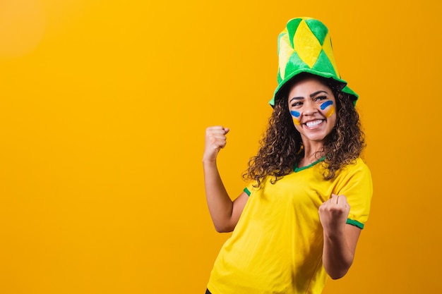 Torcedor brasileiro. fã da mulher brasileira comemorando no futebol ou jogo de futebol em fundo amarelo. cores do brasil. sim!