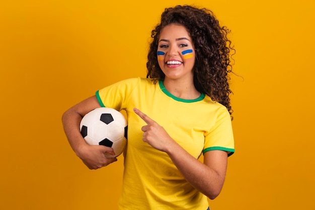 Torcedor brasileiro fã de mulher brasileira comemorando no futebol ou partida de futebol em fundo amarelo cores do brasil apontando
