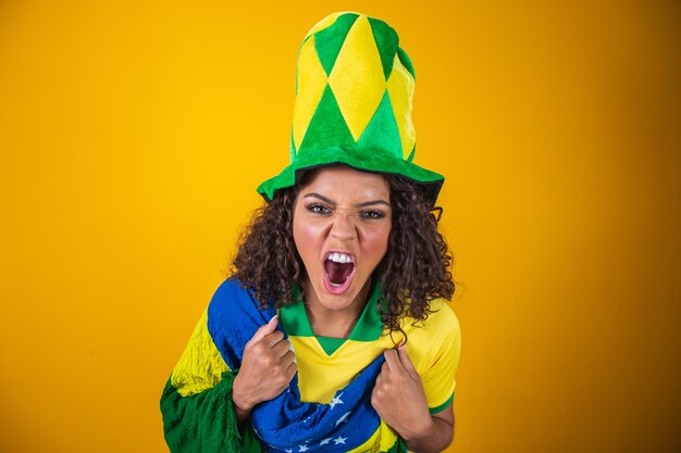 Torcedor do Brasil. Fã de mulher brasileira de cabelo encaracolado comemorando no futebol, jogo de futebol em fundo amarelo. Cores do Brasil.
