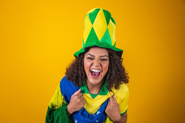 Torcedor do brasil. fã de mulher brasileira de cabelo encaracolado comemorando no futebol, jogo de futebol em fundo amarelo. cores do brasil.