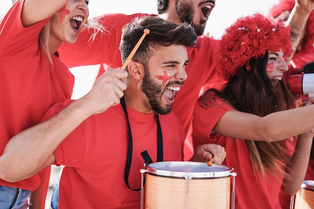 Torcedores loucos de futebol tocando bateria e gritando enquanto apoiam seu time - foco no rosto do homem