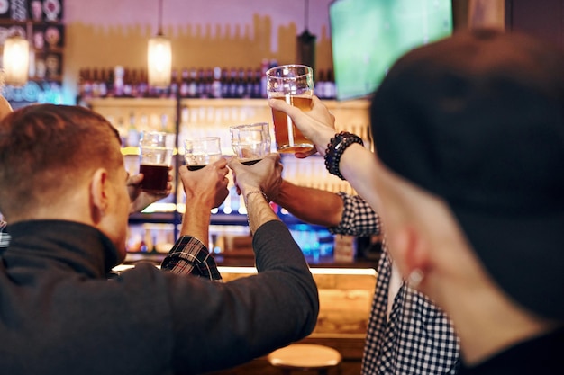 Torcendo batendo copos de cerveja Grupo de pessoas dentro de casa no pub se divertem no fim de semana