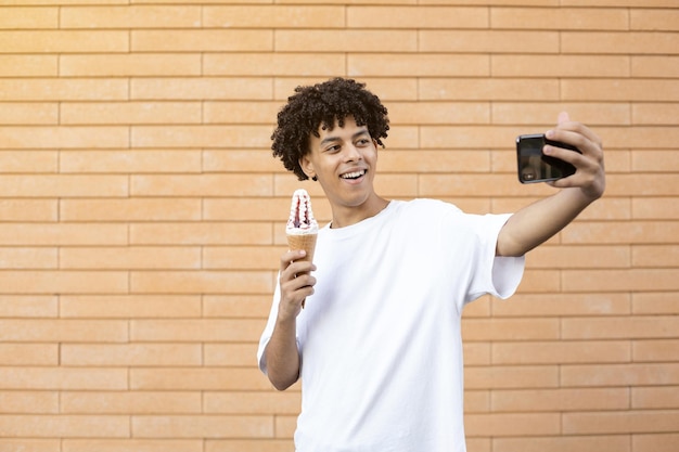 Torcendo negro segurando uma casquinha de sorvete branca com geléia vermelha e tirando selfies no telefone