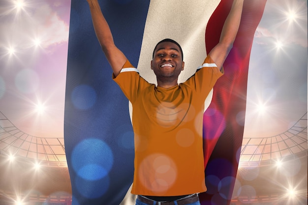 Foto torcendo pelo fã de futebol holandês em camisa laranja contra um grande estádio de futebol sob o céu azul brilhante