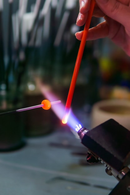 Torchworking haciendo perlas de vidrio en un taller de soplado de vidrio utilizando un quemador de alta temperatura