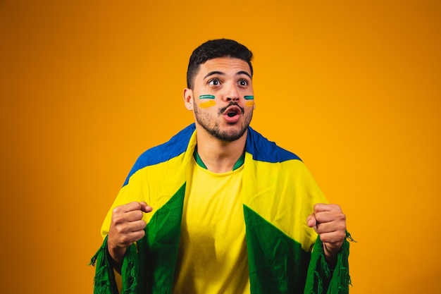 Foto torcida brasileira torcendo no meio da multidão em fundo amarelo.