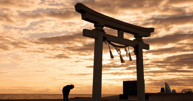 Torii portão pôr do sol céu no Japão e homem em silhueta com nuvens zen e história espiritual em viagem aventura arquitetura xintoísta cultura da noite asiática e natureza calma em monumento sagrado japonês