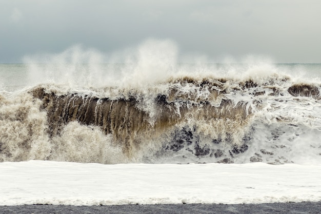 Tormenta en el mar: una gran ola de arena y espuma se eleva cerca de la orilla.