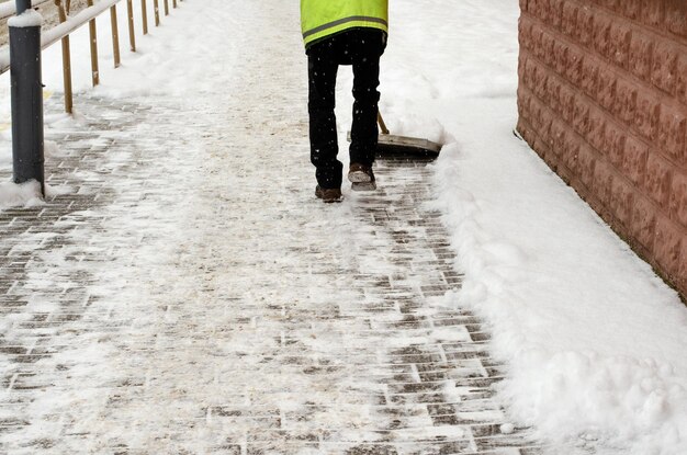 Tormenta de nieve en la ciudad Carreteras y aceras cubiertas de nieve La pala del trabajador limpia la nieve Mal clima invernal Limpieza de calles después de la tormenta de nieve