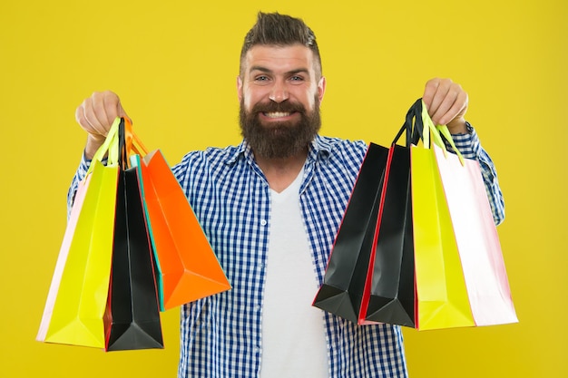 Torne as compras mais alegres. Cara alegre de hipster barbudo homem carregar sacolas de papel em fundo amarelo. Aproveite as ofertas lucrativas de compras na Black Friday. Compras com desconto, aproveite a compra.