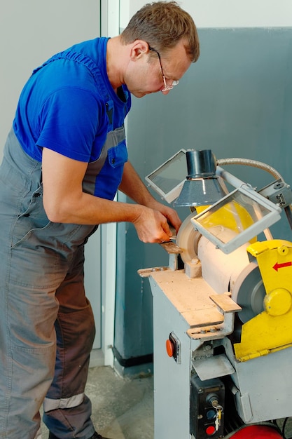 Un tornero adulto con gafas y mono de trabajo trabaja en la máquina Escena auténtica Flujo de trabajo real en el taller de torneado
