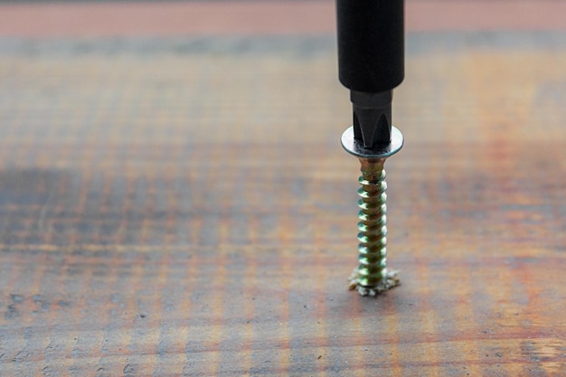 Foto tornillo de metal atornillado en la superficie de la placa de madera oscura con un destornillador negro concepto de reparación en el hogar o en el taller