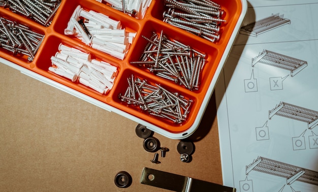 Tornillos y enchufe de pared en caja de plástico naranja Caja de herramientas de vista superior sobre fondo marrón con instrucciones de montaje de rejilla de secado de platos