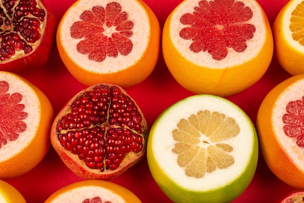 Toronja jugosa, naranja, granada, dulzura cítrica sobre fondo rojo.