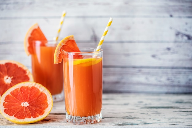 Toronjas frescas y dos vasos de jugo de toronja en la mesa de madera clara. Con espacio de copia.