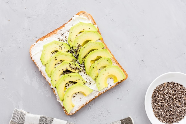 Torrada com abacate fresco, queijo creme e sementes de chia em concreto cinza