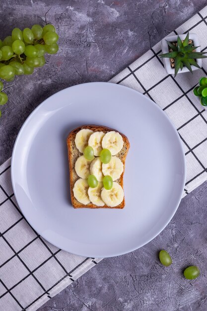 Torrada crocante com banana e uva em uma refeição saudável de fundo cinza