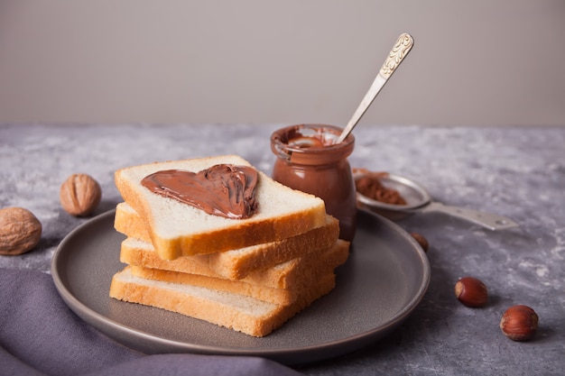 Torrada de pão com manteiga de creme de chocolate em forma de coração, pote de creme de chocolate no concreto